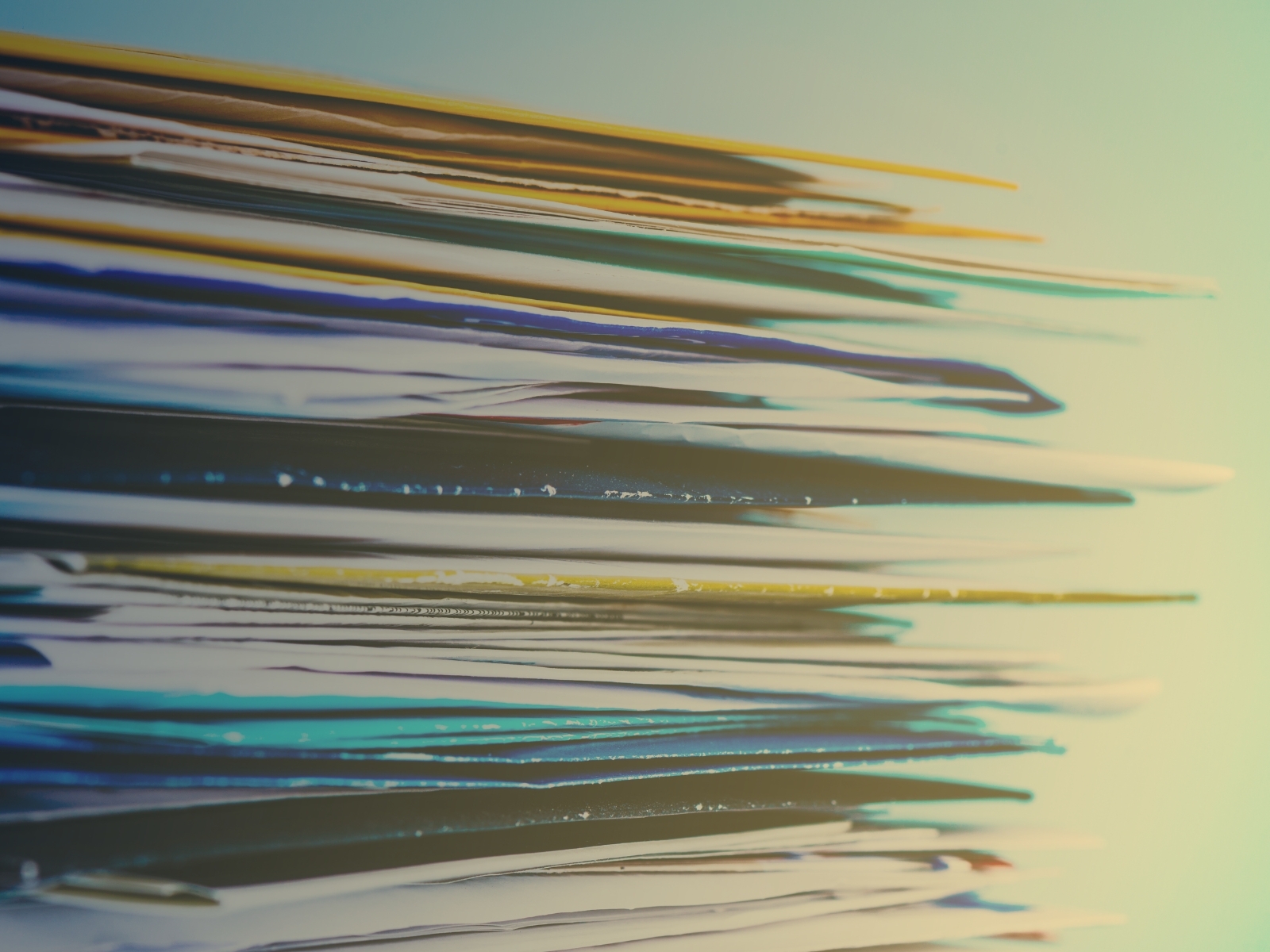 A close-up side view of a colorful stack of papers, with shades of blue, yellow, and white. The image conveys a sense of organization and productivity.