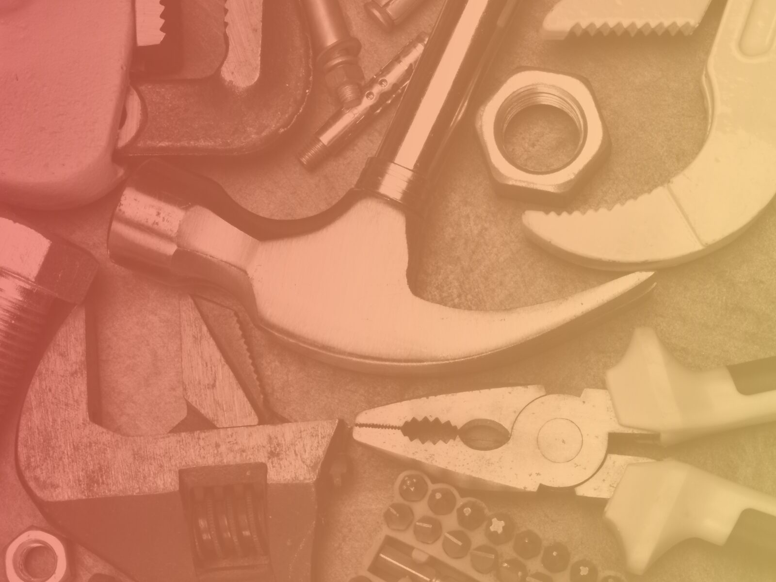 A collection of tools, including a hammer, pliers, wrench, bolts, and nuts, are scattered on a surface with a warm, reddish-orange tint.
